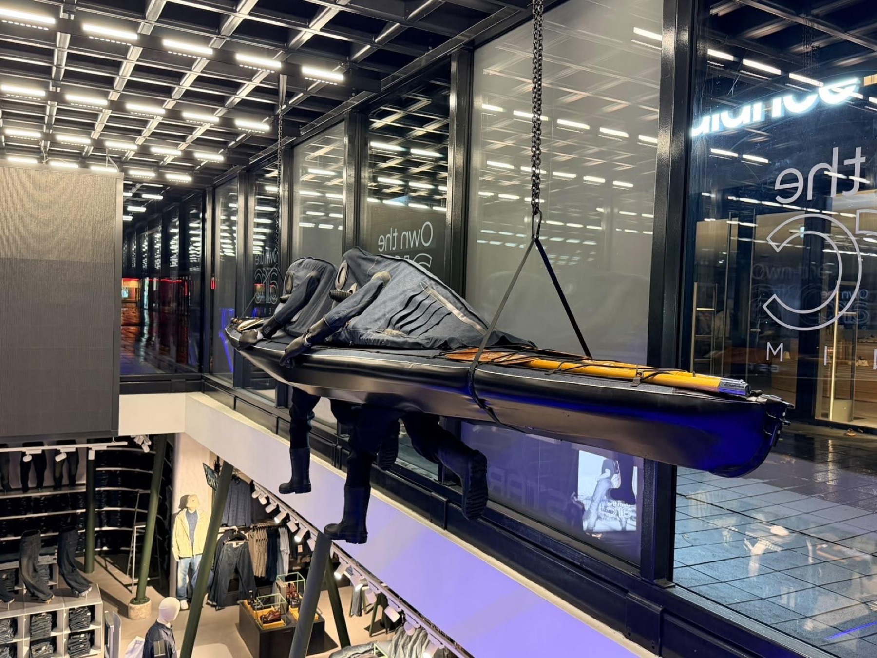 Denim-clad figures in a kayak hanging above the shop floor